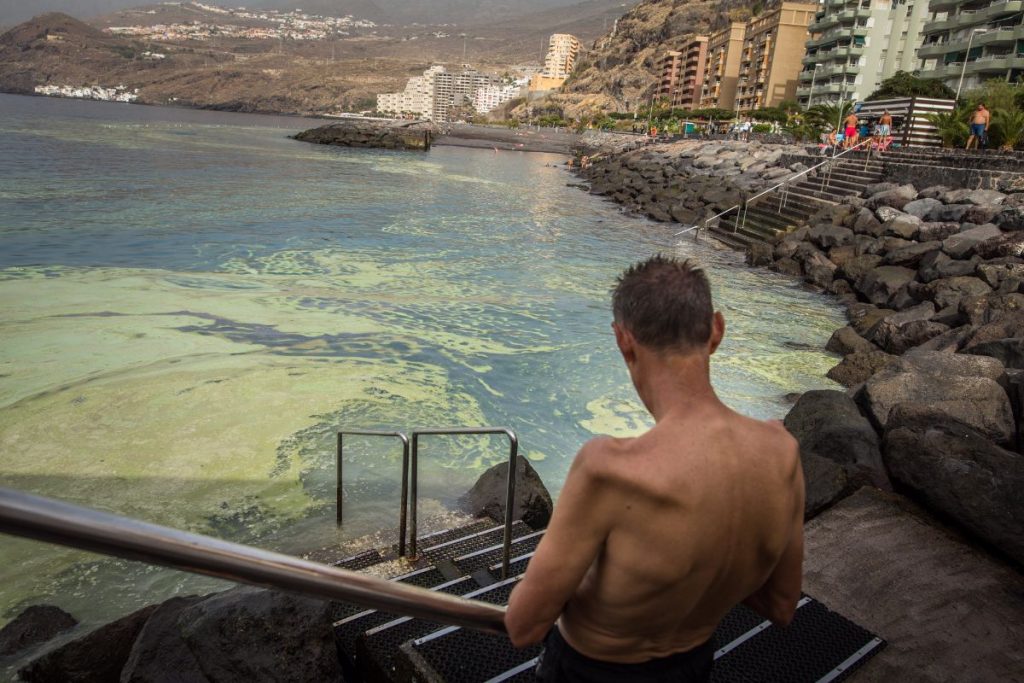 Unos bañistas, ayer, en Radazul, con las manchas de cianobacterias frente a ellos. Andrés Gutiérrez