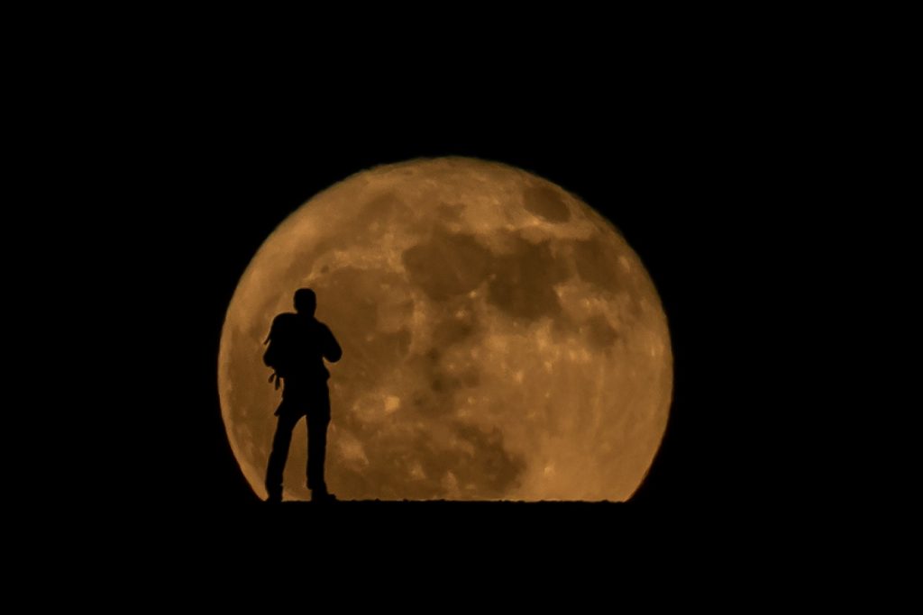 Excursionista sobre un montículo en el Parque Nacional del Teide con la Luna al fondo / Foto: Edson Vandeira