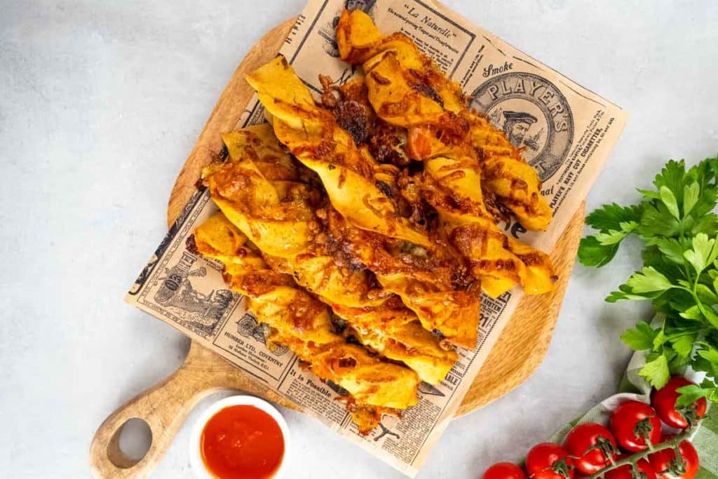 Foto de unos rollitos de pizza servidos sobre una tabla acompañados de salsa