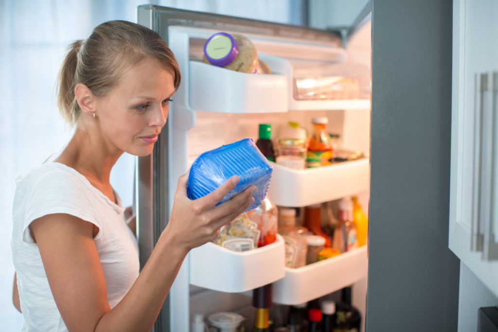 Una mujer coge alimentos de un recipiente de la nevera